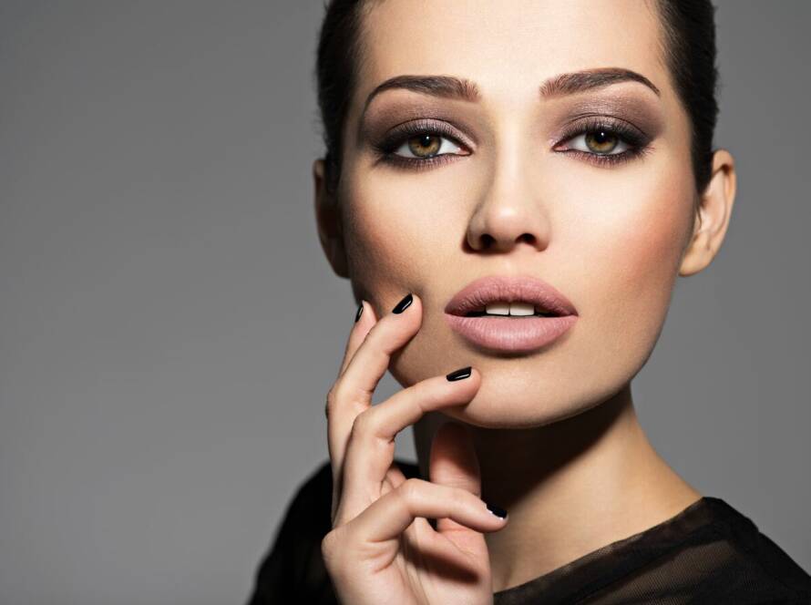 Face of a beautiful girl with fashion makeup and black nails posing at studio over dark background